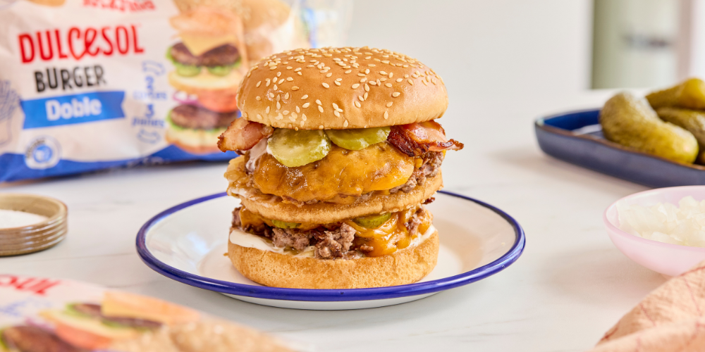 Te presentamos la hamburguesa doble Dulcesol: jugosa, con queso fundido, bacon crujiente y pepinillos agridulces.